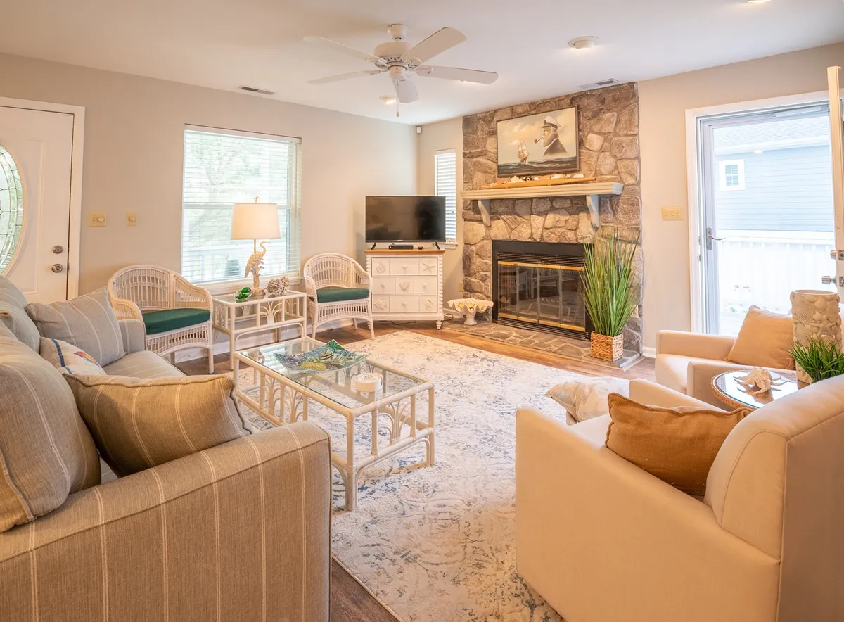 A cozy living room scene featuring a fireplace, a comfortable sofa, a coffee table set for gathering, and a television. Artwork adorns the walls, creating a welcoming atmosphere ideal for relaxing and spending time with loved ones.