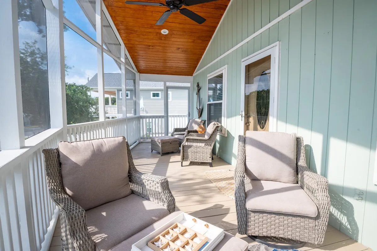This exterior image captures a sun-dappled porch scene with comfortable seating and decorative items. Sunlight streams in, creating a welcoming and casual atmosphere perfect for coffee or evening gatherings. The arrangement emphasizes both comfort and the connection to the outdoors.