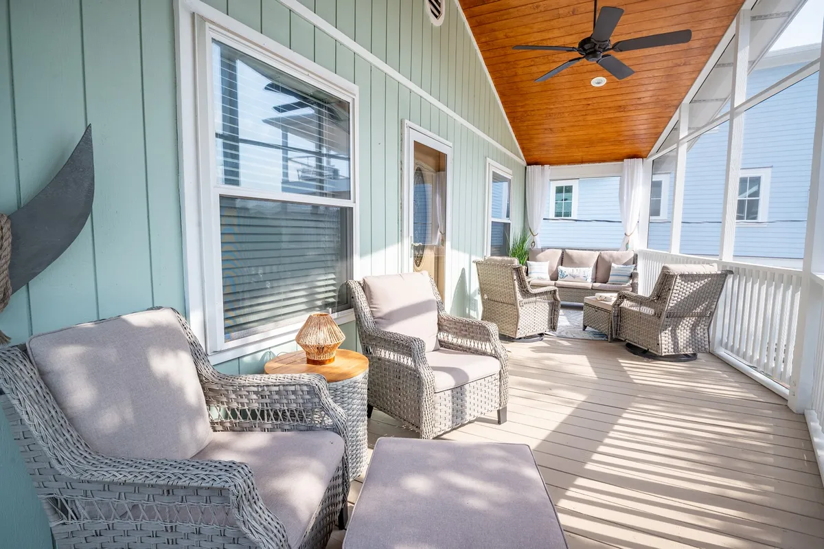 This image presents a cozy, covered porch area with woven chairs, a wooden ceiling, and decorative lanterns. The green wall and comfortable seating evoke a relaxing outdoor living room atmosphere ideally suited for gathering, sipping coffee, or sharing stories. The setup suggests protection from the sun while still being immersed in the outdoors.