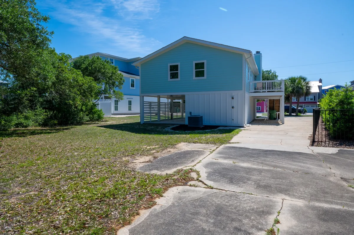 This image highlights the blue house set among greenery, with a visible driveway and open yard. The scene suggests space for parking, outdoor gatherings, and activities like barbecues or playtime, capturing the spirit of breezy backyard meals and local adventure.
